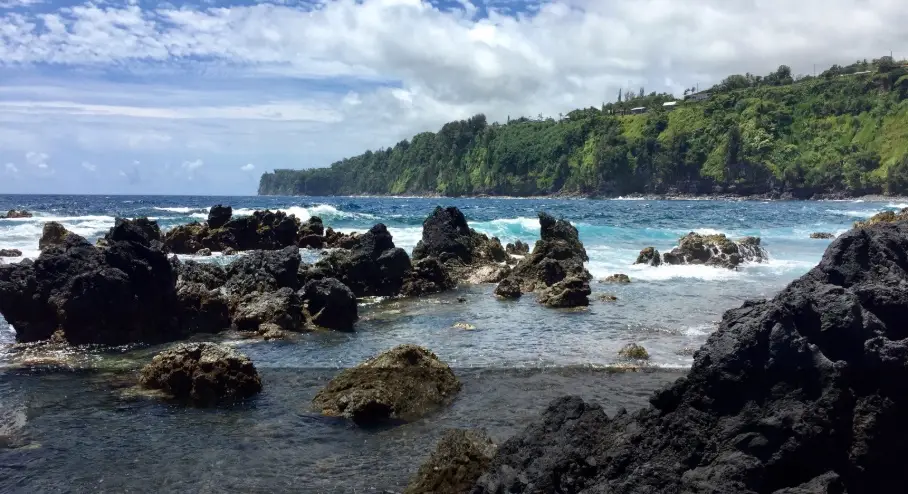 Waves breaking over lava rocks and tide pools at Laupāhoehoe Point, with sea cliffs along the Hāmākua Coast.