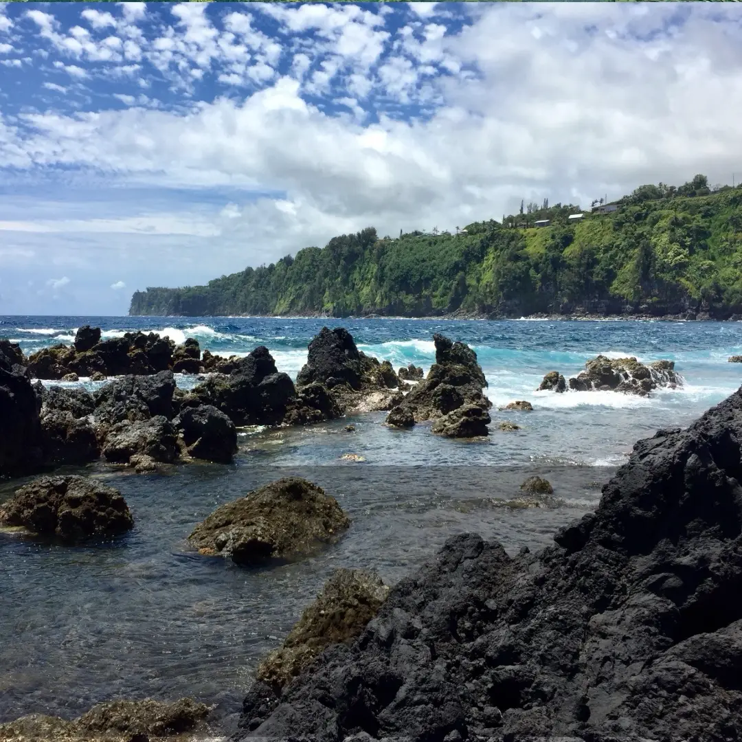 Waves breaking over lava rocks and tide pools at Laupāhoehoe Point, with sea cliffs along the Hāmākua Coast.