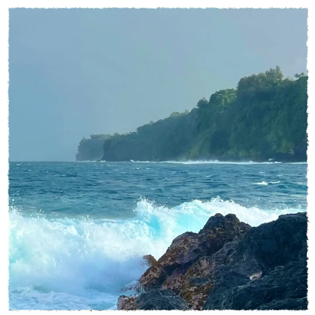 Waves crashing against volcanic rock at Laupāhoehoe Point with a rainbow over the Hāmākua Coast, Big Island of Hawaiʻi.