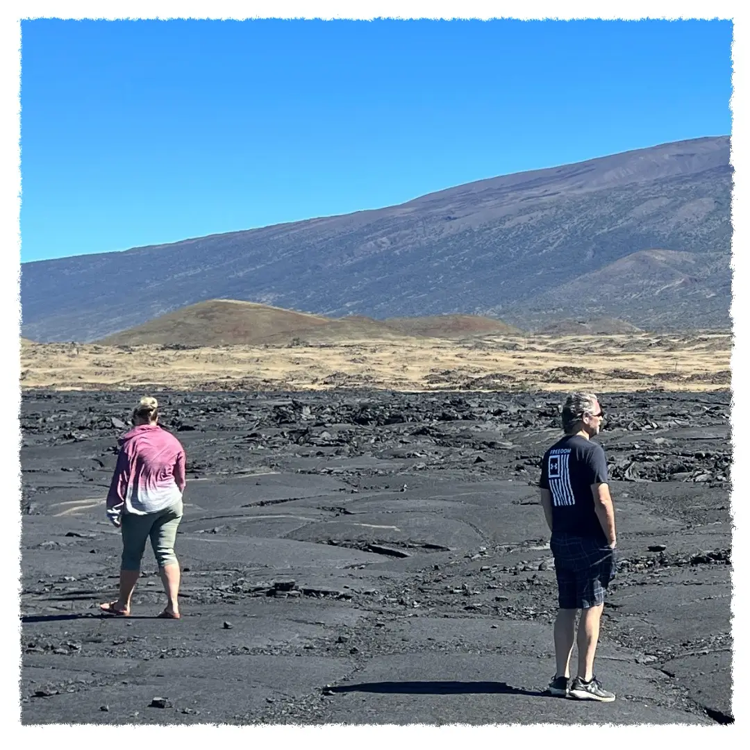 Guests walking across Mauna Loa lava fields near Saddle Road, with Mauna Kea rising in the background on a Big Island volcano tour