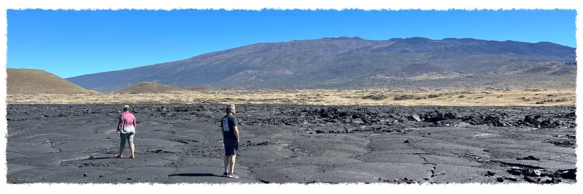 Guests walking across Mauna Loa lava fields near Saddle Road, with Mauna Kea rising in the background on a Big Island volcano tour